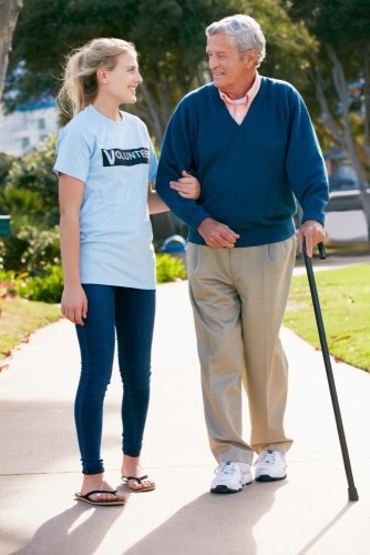 Teenage Volunteer Helping Senior Senior Man Walking Through Park